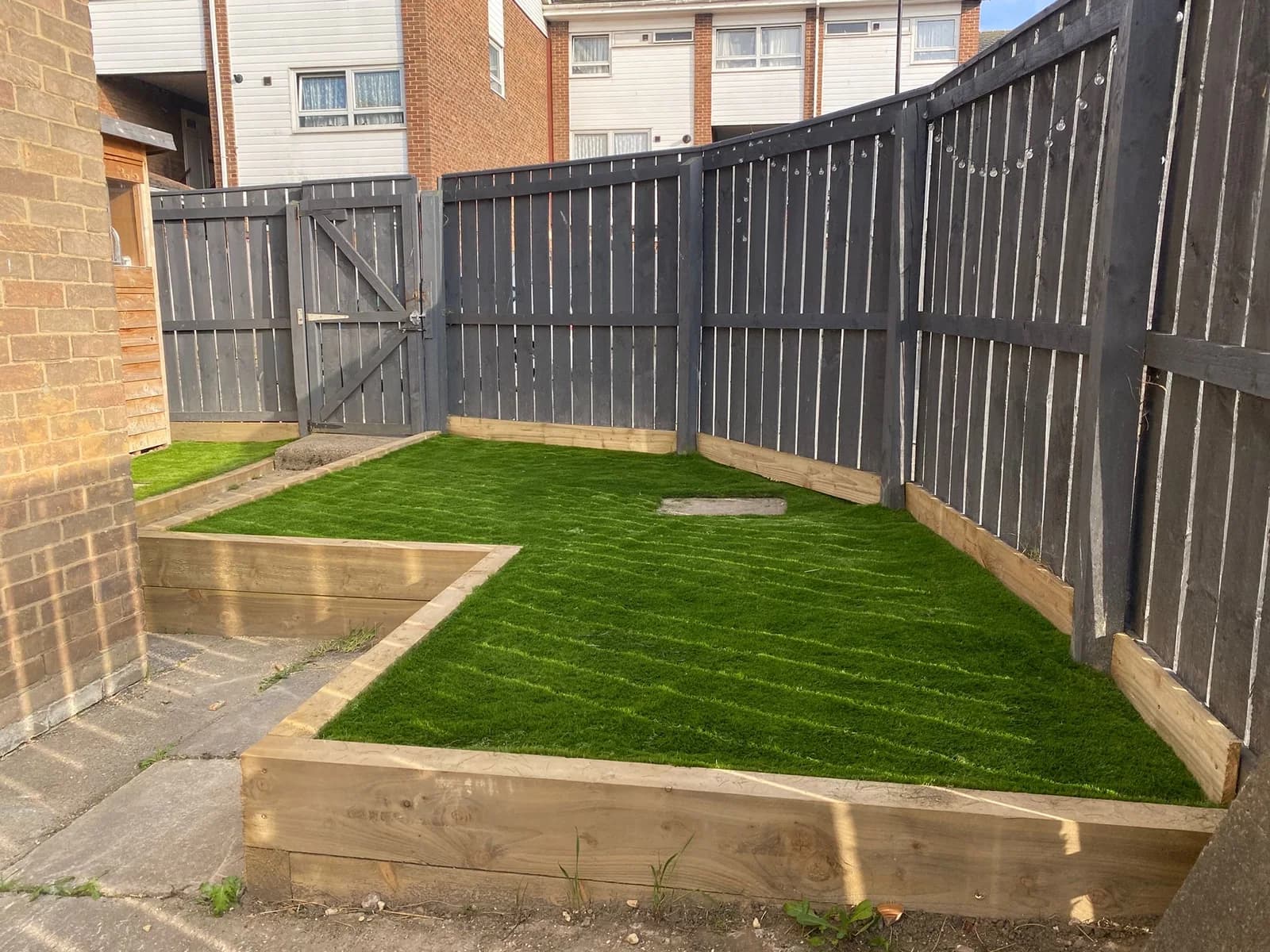 After: a usable garden with a new lawn, timber borders and a tidied fence base.